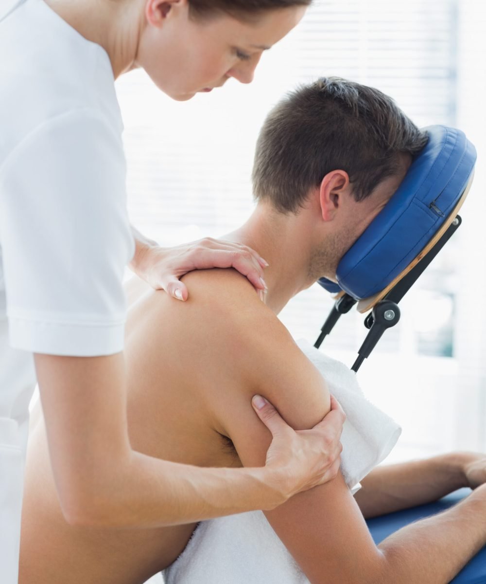 Female therapist massaging man sitting on massage chair at hospital